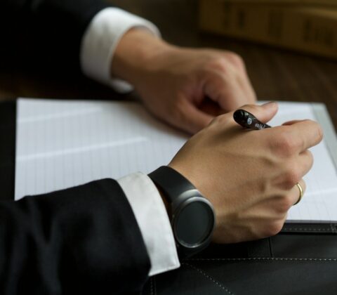 A person in a suit writing on a document.